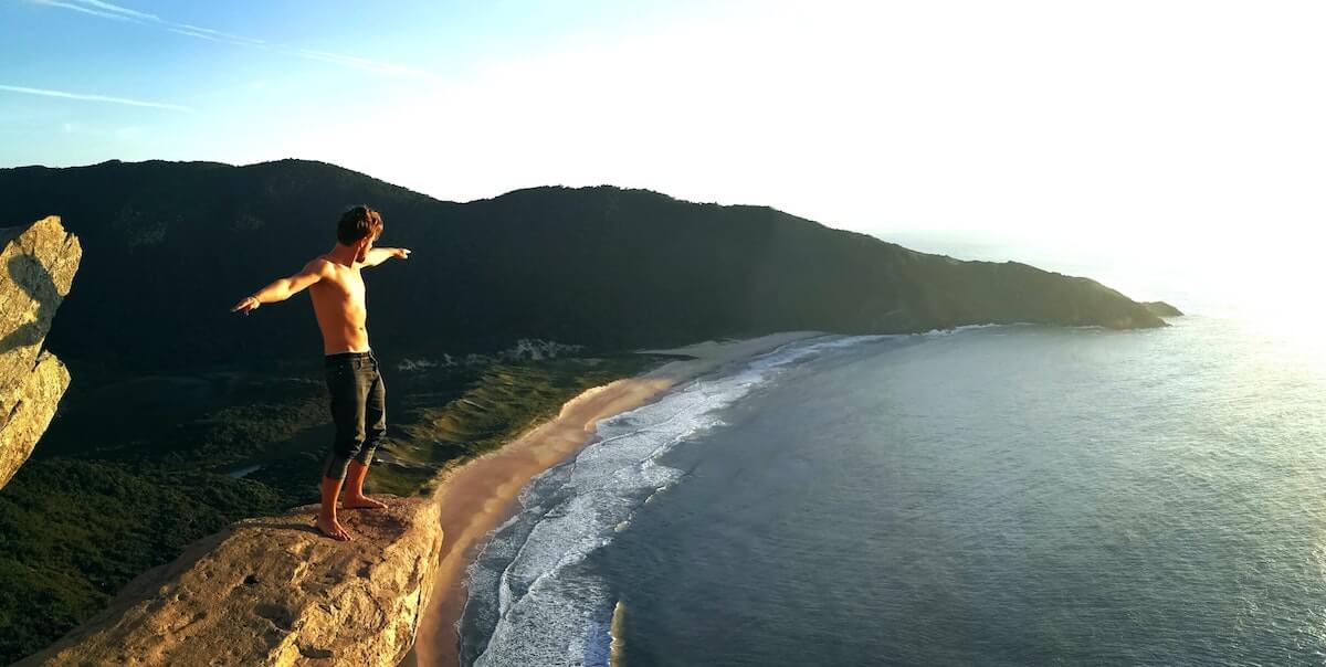 man standing on ledge with ocean below him